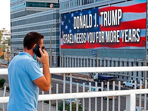 A man speaks on a cell phone while walking along a bridge near a billboard supporting US President Donald Trump in Israel's Mediterranean coastal city of Tel Aviv on October 21, 2020, less than two weeks ahead of the upcoming US presidential elections.