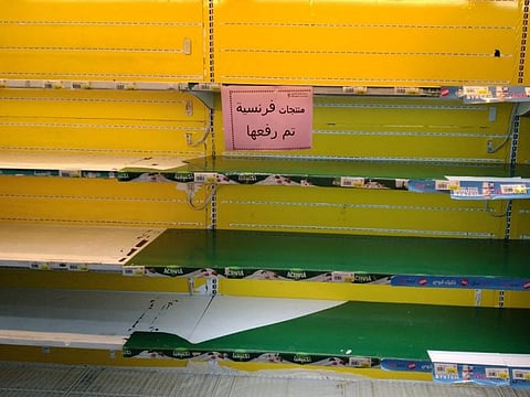 Empty shelves in a grocery store in Kuwait with a sign in Arabic reading: "French products lifted".