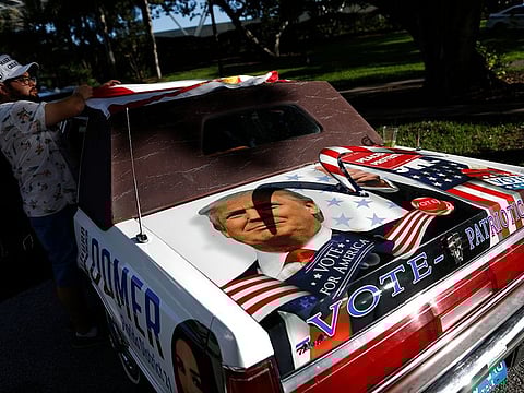 A supporter of President Donald Trump attaches a Florida flag to the top of his car, decorated with the president's image.