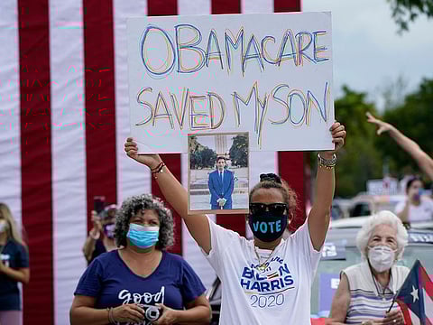 Adelys Ferro holds a sign in support of Obamacare as former President Barack Obama speaks while campaigning for Democratic presidential candidate former Vice President Joe Biden at Florida International University.