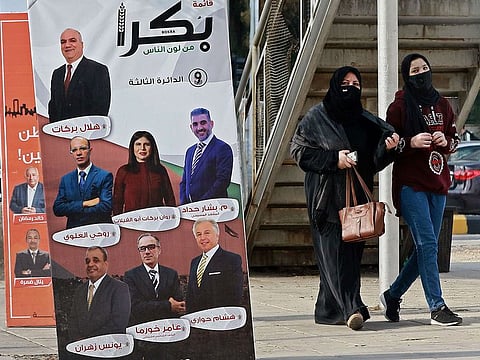 Women, mask-clad due to the COVID-19 coronavirus pandemic, walk past a campaign banner for an electoral list running in the general election scheduled for the following day, along a street in Jordan's capital Amman on November 9, 2020.