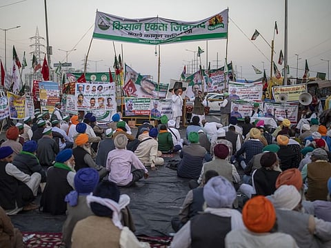 Farmers listen to a speaker, sitting in the middle of an expressway at the site of a protest against new farm laws at the Delhi-Uttar Pradesh state border, India, Wednesday, December 9, 2020.
