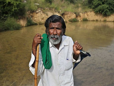 Kalmane Kamegowda, a 72-year-old shepherd, poses for a photo in front of one of the 16 ponds he created at a hillock near Dasanadoddi village, 120 kilometers (75 miles) west of Bengaluru, India, Wednesday, Nov. 25, 2020. Kamegowda, who never attended school, says he's spent at least $14,000 from his and his son’s earnings, mainly through selling sheep he tended over the years, to dig a chain of 16 ponds on a picturesque hill near his village.