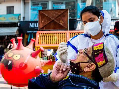 A health worker collects a swab sample from a shopper for the COVID-19 testing at a makeshift testing booth at a market area in New Delhi on December 19, 2020.