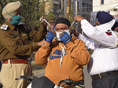 Policemen prepare to tie a mask on the face of a motorbike rider as they distribute facemasks to commuters during an awareness campaign for COVID-19 coronavirus, in Amritsar on December 20, 2020.