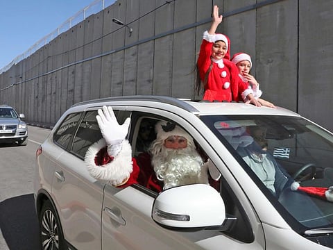 A family dressed as Santa Claus drive behind the convoy of Apostolic Administrator of the Latin Patriarchate of Jerusalem Pierbattista Pizzaballa along Israel's controversial separation barrier in the occupied West Bank town of Bethlehem on December 24, 2019.