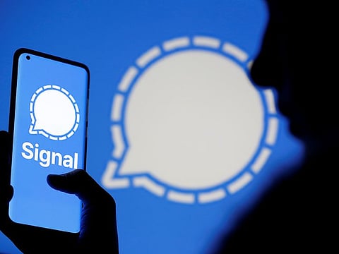A woman holds a smartphone displaying the Signal messaging app logo.