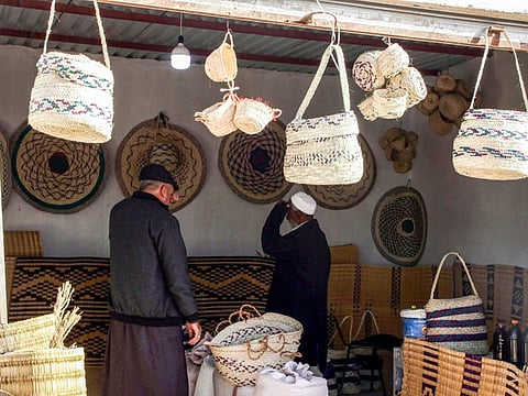 People inspect palm wicker products on display, made by Haleema Mohammed, one of the residents who returned to the city of Tawergha after fleeing in the aftermath of the toppling of Gaddafi, sits making palm wicker products at a home in Tawergha, some 200km east of Libya's capital close to the port city of Misrata, on December 12, 2020.
