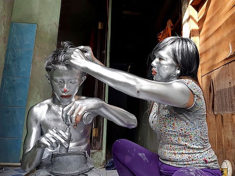 Puryanti, a 29-year-old woman, and her 15-year-old nephew Raffi, cover themselves from head to toe in silver paint to become 'manusia silver' (silver people), as part of their act to make a living, in Depok, on the outskirts of Jakarta, Indonesia.