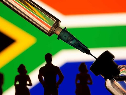 A vial, syringe and small toy figures are seen in front of displayed South Africa flag in this illustration