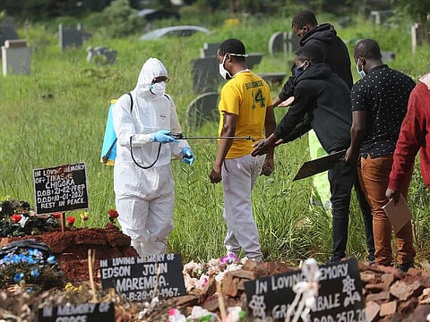 In this Jan. 15, 2021, file photo, a health worker disinfects family members during a burial of a person who died from COVID-19, in Harare, Zimbabwe. Africa has surpassed 100,000 confirmed deaths from COVID-19.