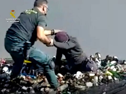 An officer of the Guardia Civil helps a man out from under glass bottles in a container in Melilla.