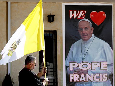 A Christian priest holds a Vatican flag as he walks by a poster of Pope Francis during preparations for the Pope's visit in Mar Youssif Church in Baghdad.