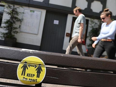 People walk past a sign promoting social distancing placed on a bench following a spike in cases of the coronavirus disease (COVID-19) in Stone, Britain.