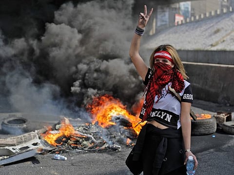 A bandana-clad anti-government demonstrator gestures as she stands by the smoke of burning tyres at a make-shift roadblock in Zouk Mosbeh north of Lebanon's capital Beirut, on March 8, 2021 during a protest against the deteriorating value of the local currency and dire economic and social conditions.
