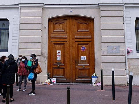 People stand next to flowers and messages laid at the entrance of the Cognacq-Jay highschool in Argenteuil, on the outskirts of Paris, on March 10, 2021, in tribute to the 14-year-old schoolgirl whose beaten body was found two days before in the Seine river