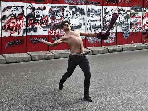 A protester throws stones towards the central bank building in Beirut, Lebanon, Saturday, March. 13, 2021.
