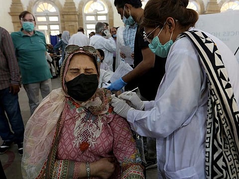 A woman reacts while receiving a Sinopharm coronavirus vaccine from a health worker at a vaccination centre, in Karachi, Sindh on March 16, 2021.