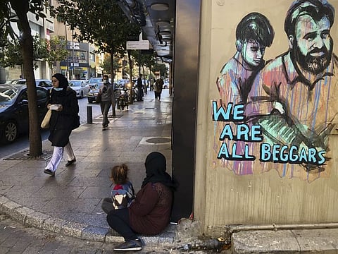 People pass next of a woman, centre, who is sits on the ground with her daughter begging on Beirut's commercial Hamra Street on March 16, 2021. More than half the population now lives in poverty, while an intractable political crisis heralds further collapse and Lebanese are gripped by fear for the future.