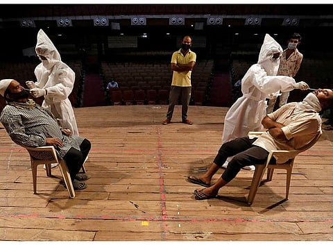 Healthcare workers wearing personal protective equipment (PPE) collect swab samples from men during a rapid antigen testing campaign for the coronavirus disease (COVID-19), at an auditorium turned into a testing centre in Ahmedabad, India, March 23, 2021.