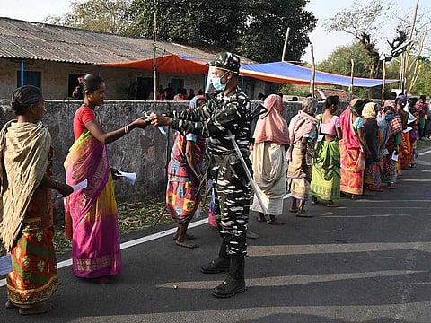 A paramilitary personnel distributes facemasks to voters standing in queue to cast their ballots outside a polling station during Phase 1 of West Bengal's legislative election in Purulia district on March 27, 2021.