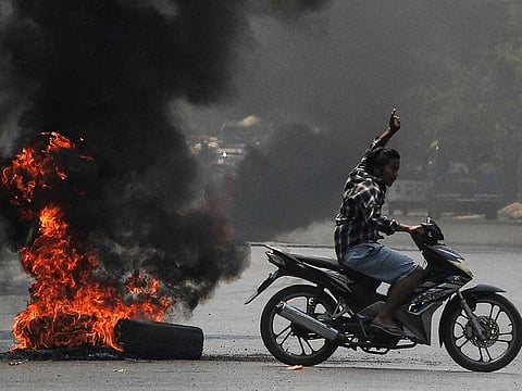 A man flashes the three-finger salute as he passes burning tires during a protest against the military coup, in Mandalay, Myanmar April 1, 2021.