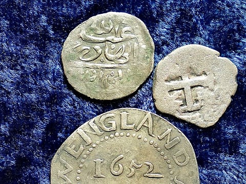 A 17th century Arabian silver coin, top, that research shows was struck in 1693 in Yemen, rests near an Oak Tree Shilling minted in 1652 by the Massachusetts Bay Colony, below, and a Spanish half real coin from 1727, right, on a table, in Warwick, R.I., Thursday, March 11, 2021.