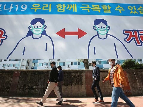 People wearing face masks pass by a banner displaying precautions against the coronavirus on a street in Seoul, South Korea, Monday, April 5, 2021. The banner reads " We can overcome Corona 19."