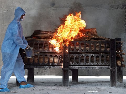 A frontline worker in personal protective equipment (PPE) sprays a flammable liquid on a burning funeral pyre of a man who died from COVID-19, at a crematorium on the outskirts of Mumbai.
