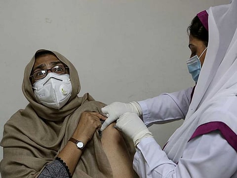 A woman reacts while receiving the second shot of the Sinopharm COVID-19 vaccine from a health worker at a vaccination centre, in Peshawar, Pakistan