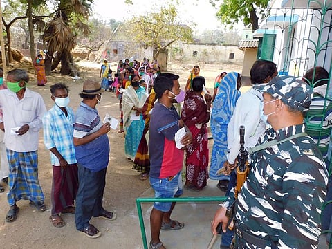 Paramilitary personnel stands guard as voters stand in a queue to cast vote during the first phase of the Assembly elections, in Bankura.