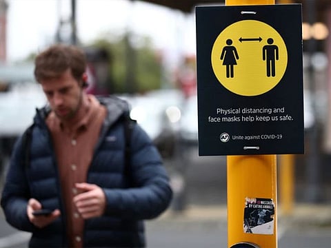 A man walks by a social distancing sign in Auckland, New Zealand.