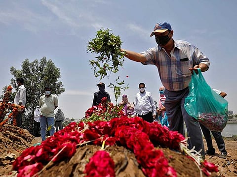 A man scatters leaves and flower petals on the grave of 65-year-old Arnold Samuel Christian, who died from the coronavirus disease (COVID-19), after his burial at a cemetery in Ahmedabad, India, May 3, 2021.