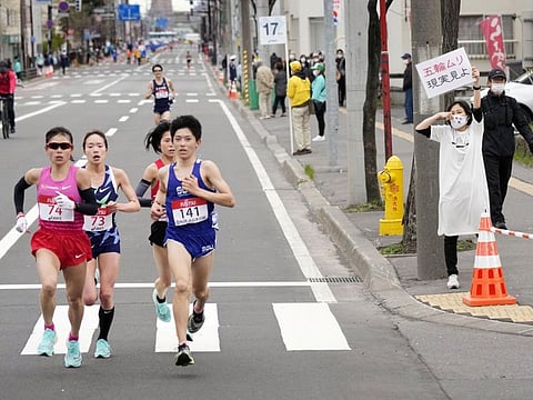 A spectator raises a paper sign reading 'It is impossible to hold the Olympics, face up to reality' along the race route during the half-marathon as part of Hokkaido-Sapporo Marathon Festival 2021, a test event for the Tokyo 2020 Olympics marathon on Wednesday.