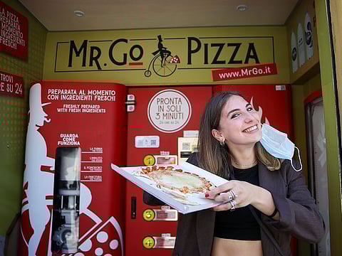 Fabrizia Pugliese poses with her order at the first automatic pizza vending machine, which is capable of kneading, seasoning and cooking the pizza in three minutes, in Rome, Italy, May 6, 2021.