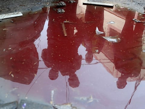 People are reflected in a puddle of water mixed with blood at the scene where Palestinians were killed amid by Israel, in the northern Gaza Strip May 10, 2021.