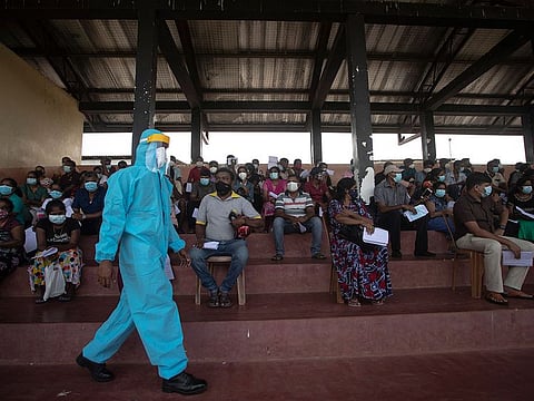 A Sri Lankan army soldier in protective suit walks past people waiting to receive a jab of Sinopharm COVID-19 vaccine at a vaccination center run by military at a playground in Colombo, Sri Lanka, Tuesday, May 11, 2021.