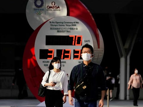 Passersby wearing protective face masks walk near a countdown clock of Tokyo 2020 Olympic Games that have been postponed to 2021 due to the coronavirus disease (COVID-19) outbreak, in Tokyo, Japan May 14, 2021.