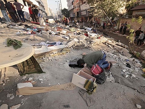 A Palestinian man listens for any sounds from under the rubble of a building, after it was struck by Israeli strikes, in Gaza on May 16, 2021.