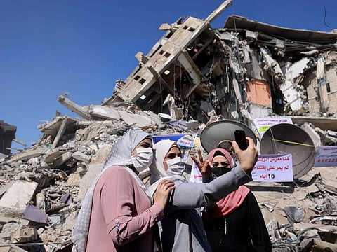 Palestinian women pose for a 'selfie' in front of a demolished building in the Al Remal commercial district in Gaza City, recently targeted by Israeli air strikes, on May 23, 2021.