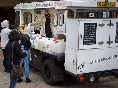 Founder of Topup Truck, Ella Shone (R) serves a customer from her electric milk float converted into a zero waste shop which brings "packaging-free" shopping to people's doors, in east London.