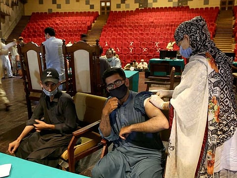 A government employee receives the COVID-19 vaccine from a health worker while others wait their turn at a vaccination centre in the Nishtar hall, in Peshawar, Pakistan, Friday, June 11, 2021.