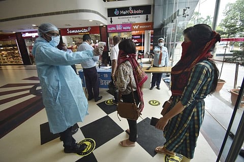 A security personnel does thermal screening of a visitor at the entrance to a mall in Gorakhpur.