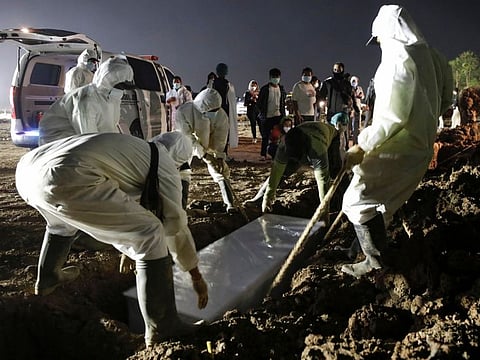 Gravediggers bury a body as relatives stand behind in Jakarta on July 7, 2021.