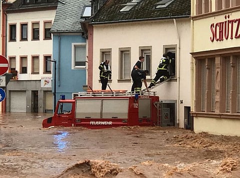 Firemen standing on the roof of their vehicle climb into an inundated house in the flooded Ehrang neighbourhood in Trier, western Germany, on July 15, 2021.