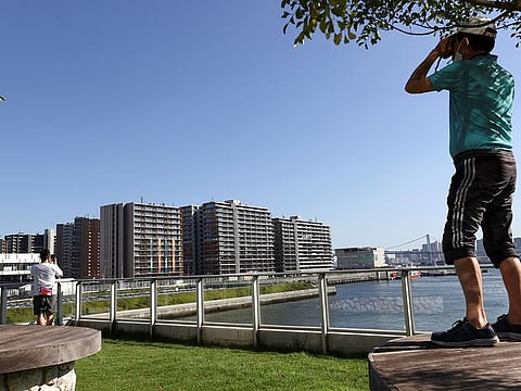 A man uses binoculars to look at the Athletes Village, where a person has tested positive for COVID-19, ahead of Tokyo 2020 Olympic Games