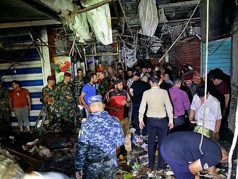 People and security forces gather at the site of a bombing in Wahailat market in Sadr City, Iraq, Monday, July. 19, 2021. A bomb attack targeted a Baghdad suburb, killing at least 30 people and wounding dozens of others at a crowded market, Iraqi security officials said.