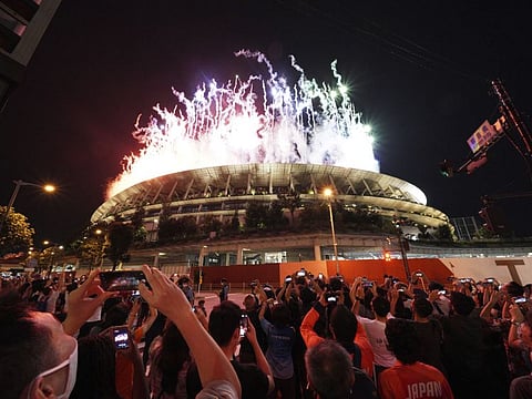 People gathered near the National Stadium watch the fireworks launched during the closing ceremony of the Tokyo Olympics in Tokyo, Japan.