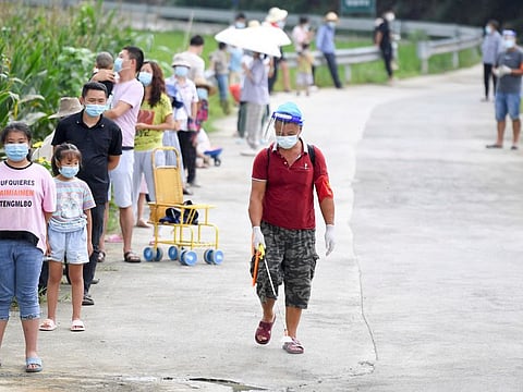 A worker disinfects next to villagers lining up by a corn field for nucleic acid testing at Baiyangping village following the coronavirus disease (COVID-19) outbreak in Zhangjiajie, Hunan province, China August 12, 2021. Picture taken August 12, 2021. cnsphoto via REUTERS ATTENTION EDITORS - THIS IMAGE WAS PROVIDED BY A THIRD PARTY. CHINA OUT.