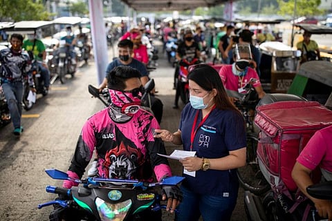 A health worker explains the information in the vaccination card to a foodpanda delivery rider after getting a jab of Sinovac in a shopping mall's parking lot turned into a drive-thru vaccination site, in Quezon City, Metro Manila, on August 13, 2021.